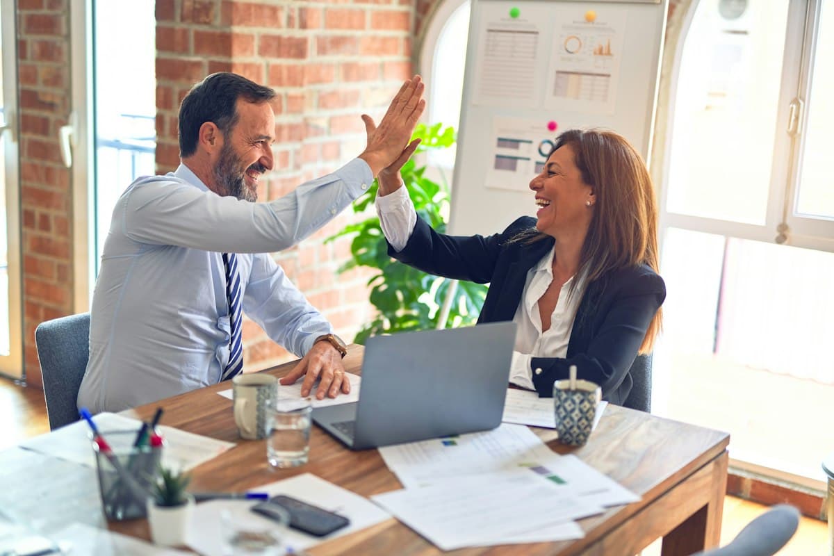 Two colleagues celebrating progress on a project at a desk with a laptop